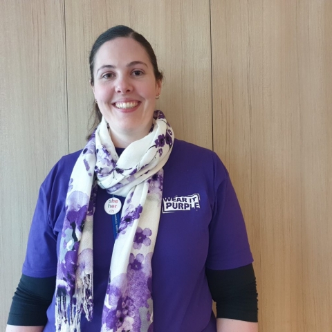 A young woman smiling while wearing a purple tshirt.