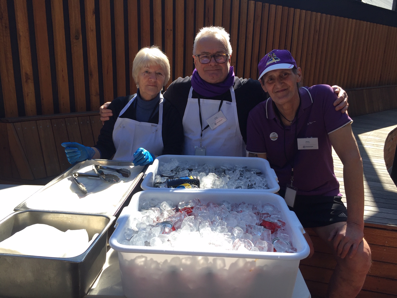 One woman and two men outdoors with box of ice and cold drinks