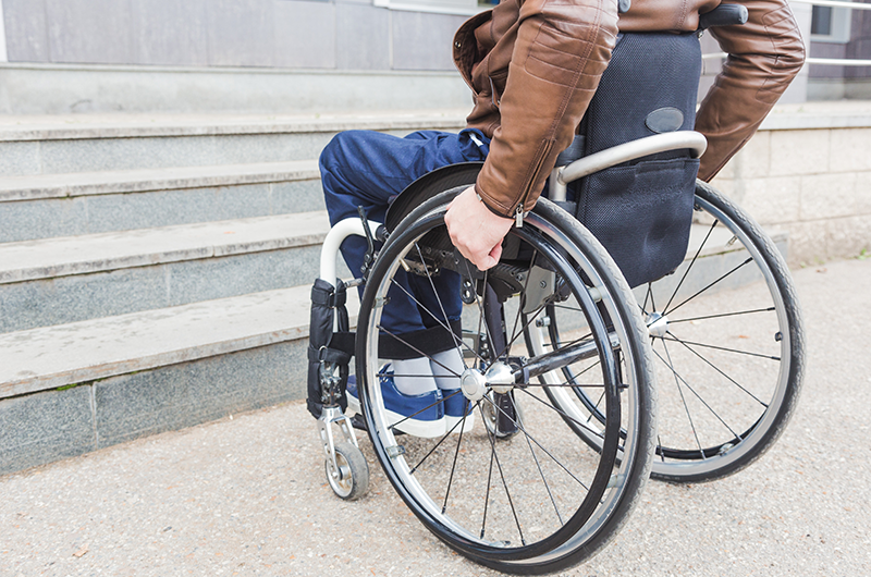 man in wheelchair in a city at the base of stairs